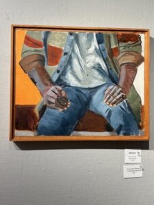The painting "Mamadou" by Wendy Goidell, depicting a seated human figure viewed from the upper chest down to the knees. The figure is wearing a plaid shirt left unbuttoned over a white undershirt and denim jeans, and has dark brown skin.